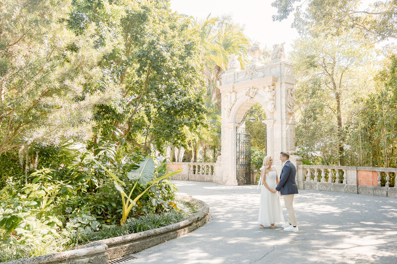 Man and woman sit next to each other on stone steps outdoors with woman's legs over man's legs during engagement photography session
