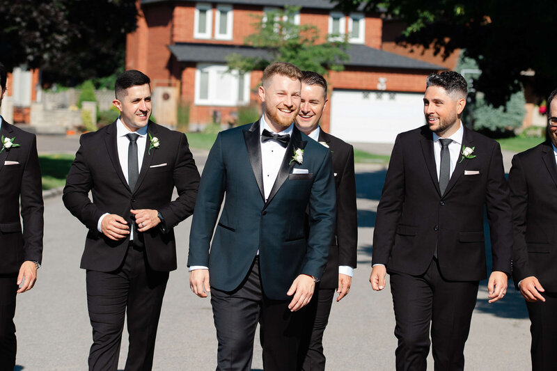 a groom and his groomsmen in black tuxedos walking and laughing.  Ottawa wedding photography by JEMMAN Photography