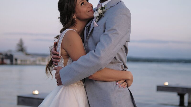 Bride looks up at groom as they are by the shore on Canandaigua Lake, standing on the docks at the Lakehouse