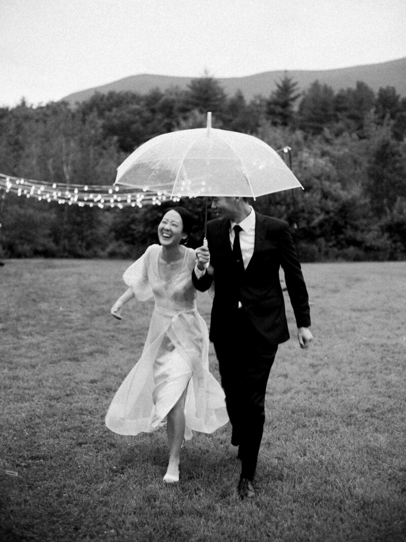 bride and groom share umbrella in the rain