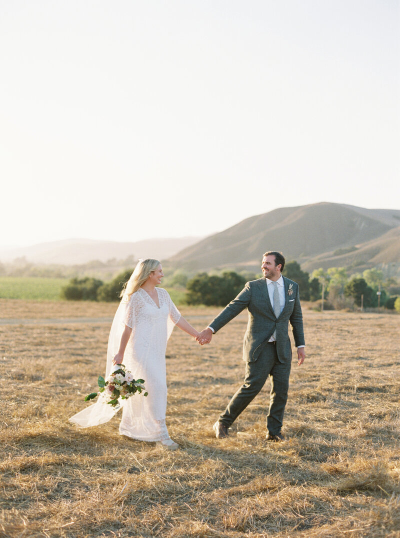 engaged couple holding hands in a field in california