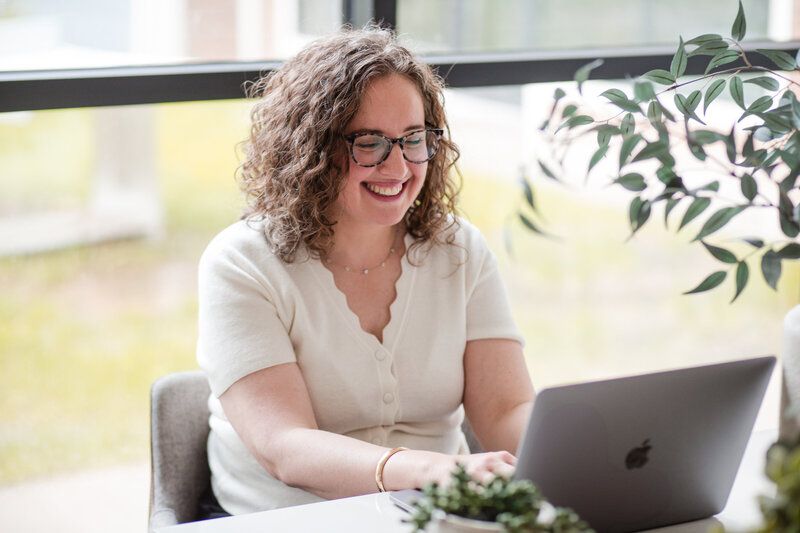 Jenn Kauffman smiling while working on her laptop during an HR consulting session, specializing in Workday implementation and strategy.