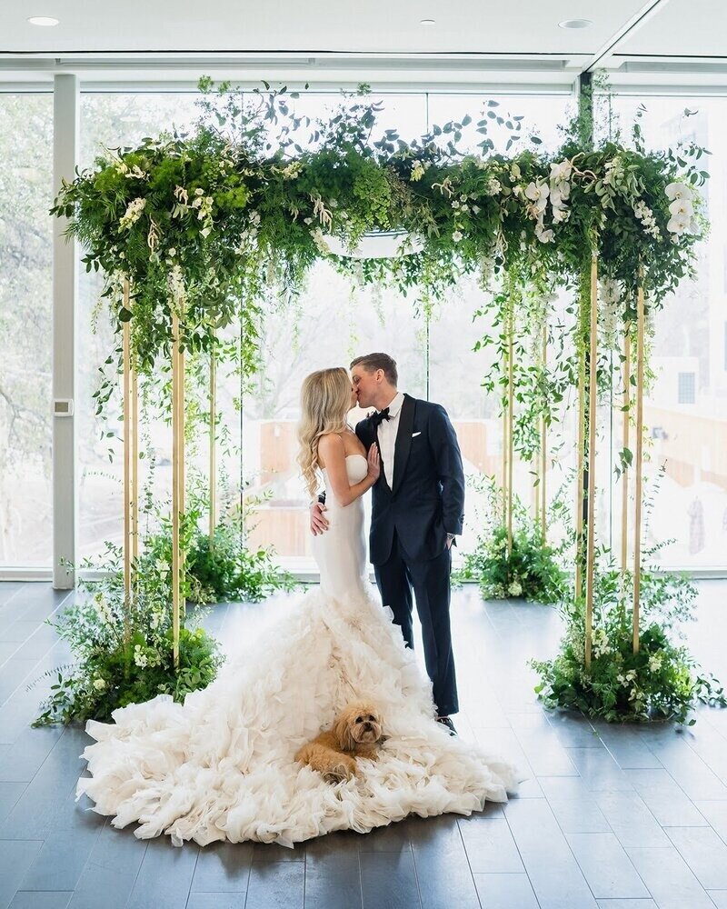 Newlyweds kissing under a chuppah designed with greenery and flowers by florists in Austin TX.