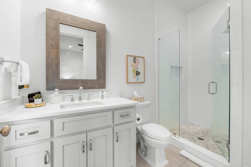 Sleek bathroom with large mirror, glass walk-in shower, and beachy artwork at Carillon Beach vacation rental.
