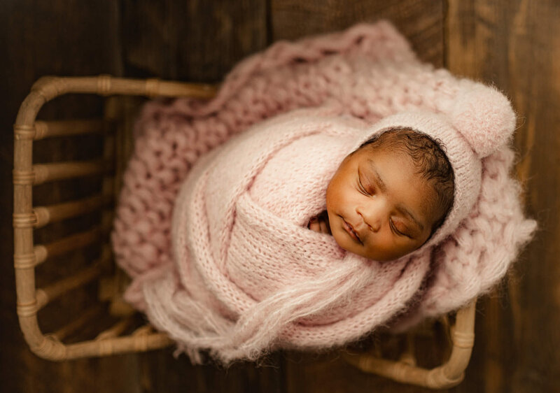 Newborn girl swaddled in pink posed in baby prop