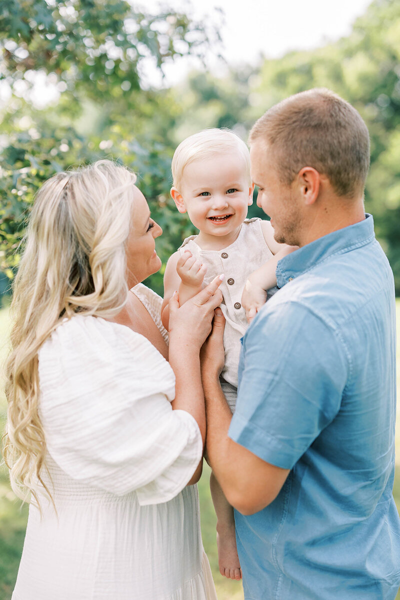 Mom and dad look lovingly at toddler son underneath a tree at a park in Mechanicsburg, PA