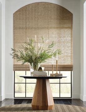 Handwoven natural woven shade on an arched window above a round wood entry table