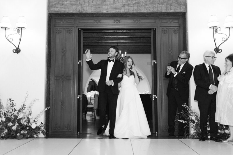 black and white image of a bride and groom grand entrance into their reception the groom waves and the bride screams captured by santa barbara wedding photographer magnolia west photography taken at the montecito club wedding