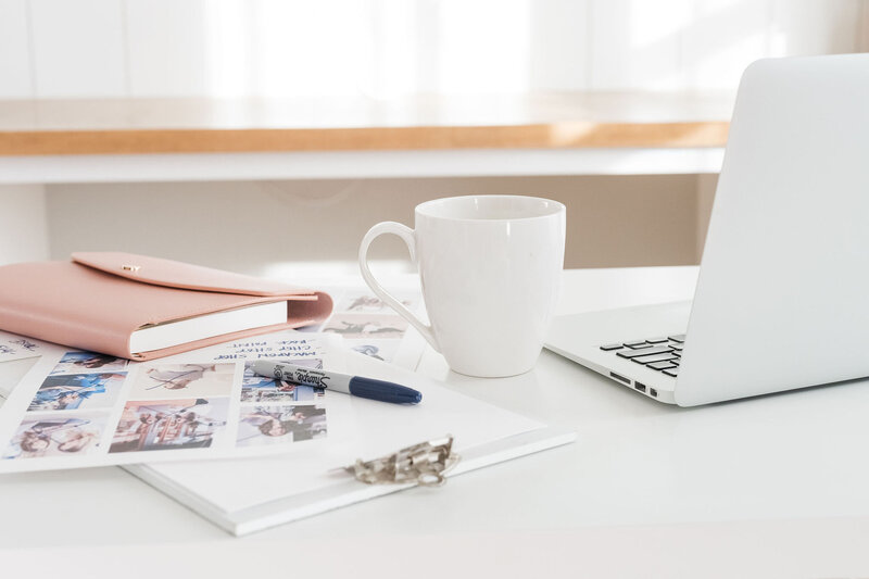 laptop, photos, pink planner on white table