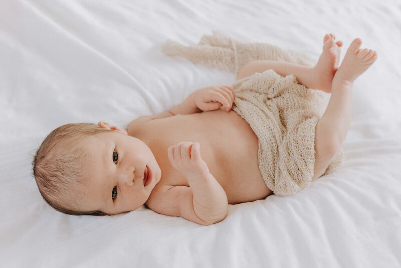 Portrait of a baby with a faint smile, wrapped in a knitted wrap. Captured with timeless simplicity by Nostalgia.