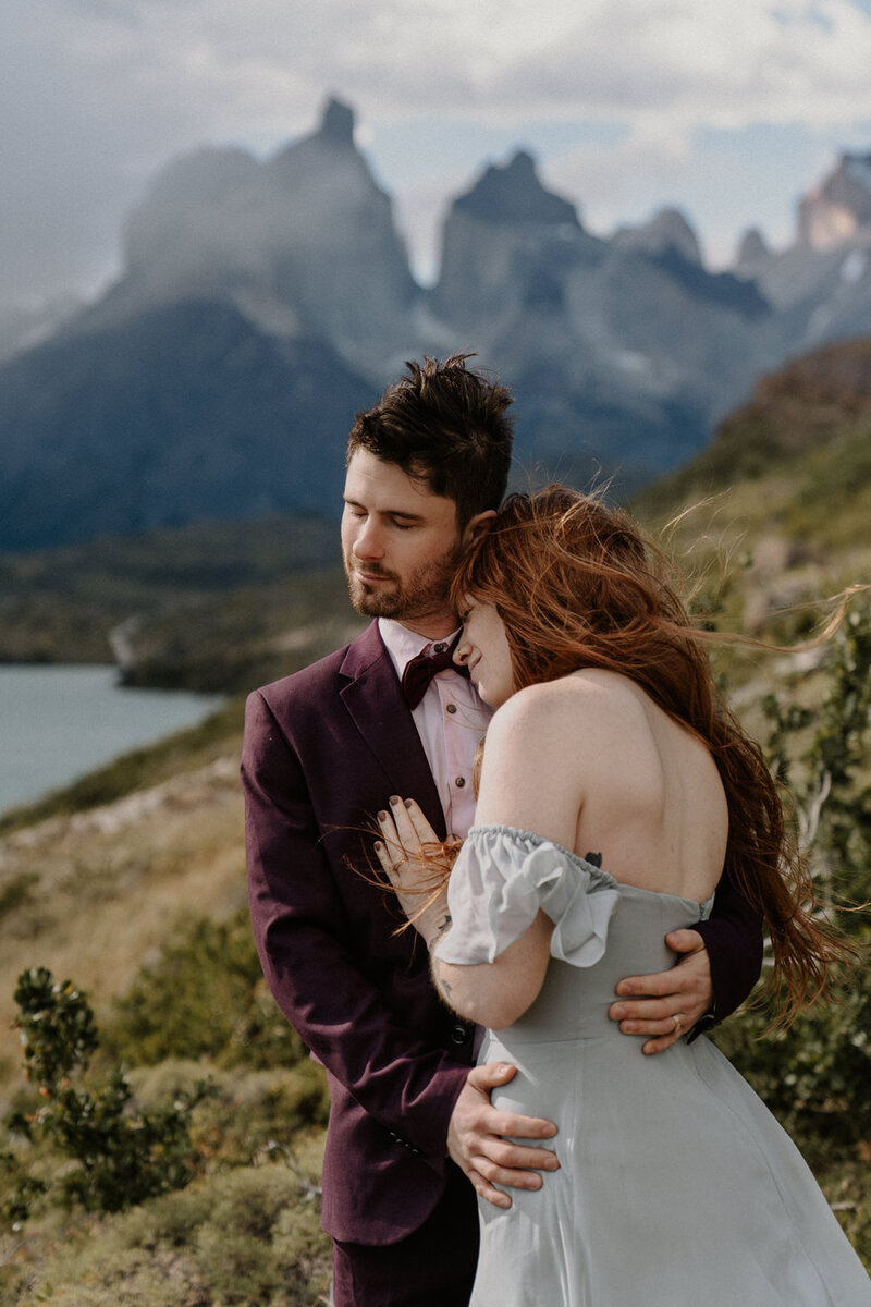 A couple. cradles each other's faces before a kiss. They are smiling with their eyes closed and the sun is shining goldem behind them.