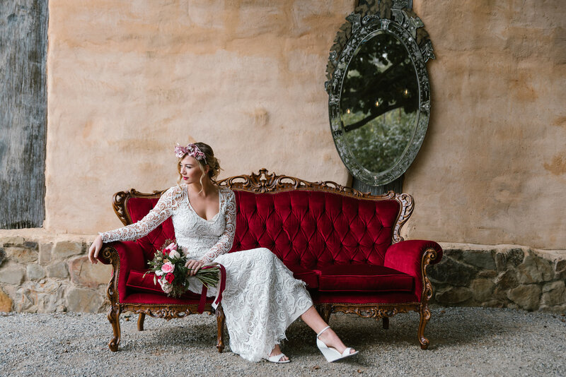 Bride in wedding dress sitting on red velvet couch at wedding reception