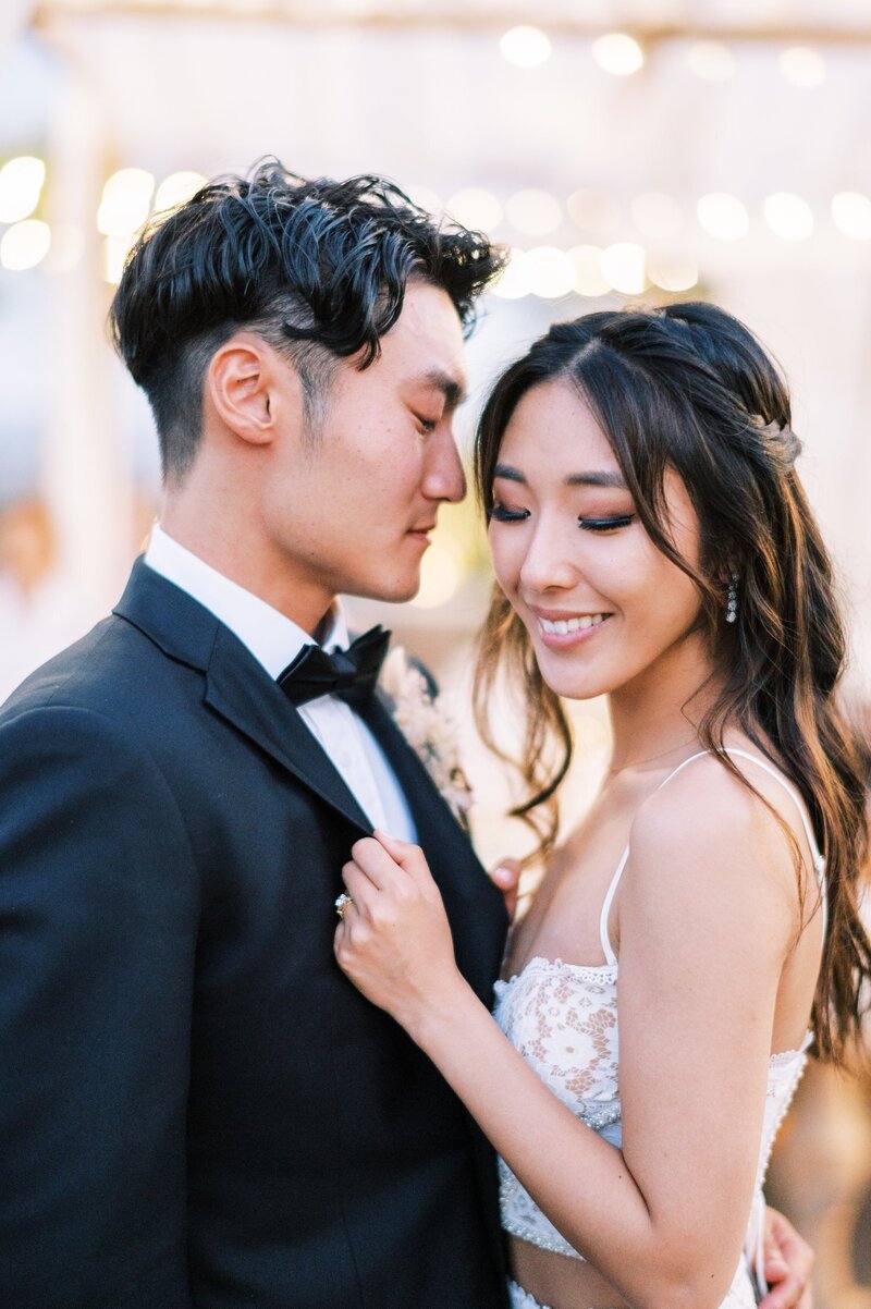 Kohnur bride with soft glam makeup and loose waves wearing a sheer gown and gold floral headpiece in an indoor studio with pink backdrop In Yorba Linda, California.