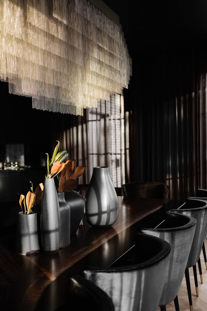A luxury dining room with an oversized gold chandelier paired with black velvet dining chairs.