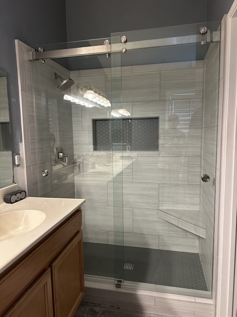 A remodeled shower with dark tile floors, light grey large tiles and brushed nickel hardware done in the Inland Empire.
