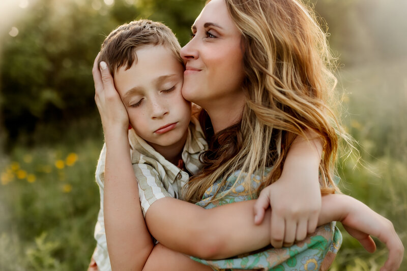 Son with closed eyes hugs his mom as she warmly embraces him in a wildflower field during family photos in Kansas City