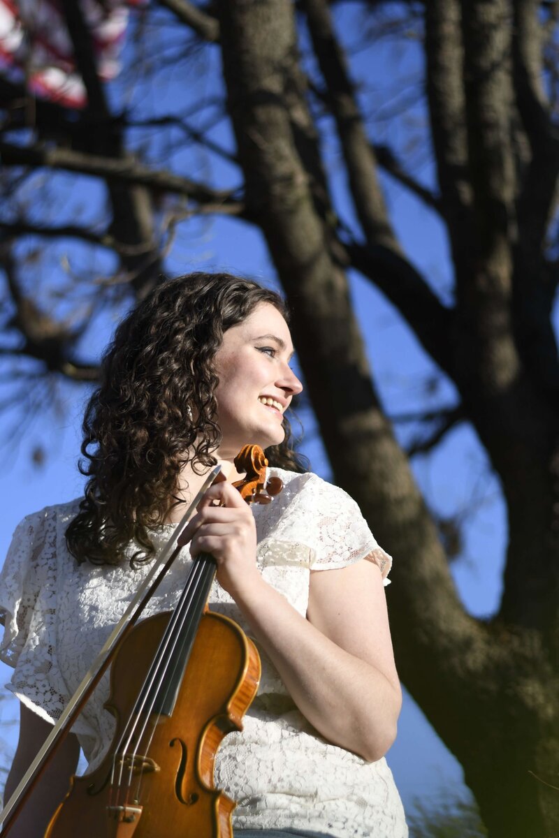 Seattle violin teacher Erika Burns sits in front of a tree looking to the side.