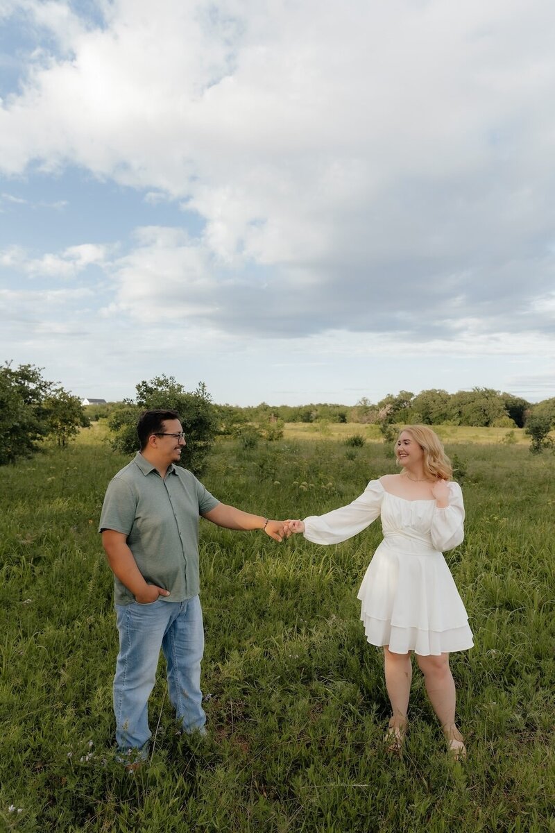 couple holds hands in field during portrait session in texas