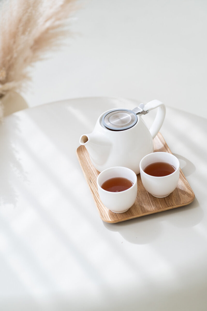 na stolečku je tác s bílou konvicí a bílými hrnečky s čajem