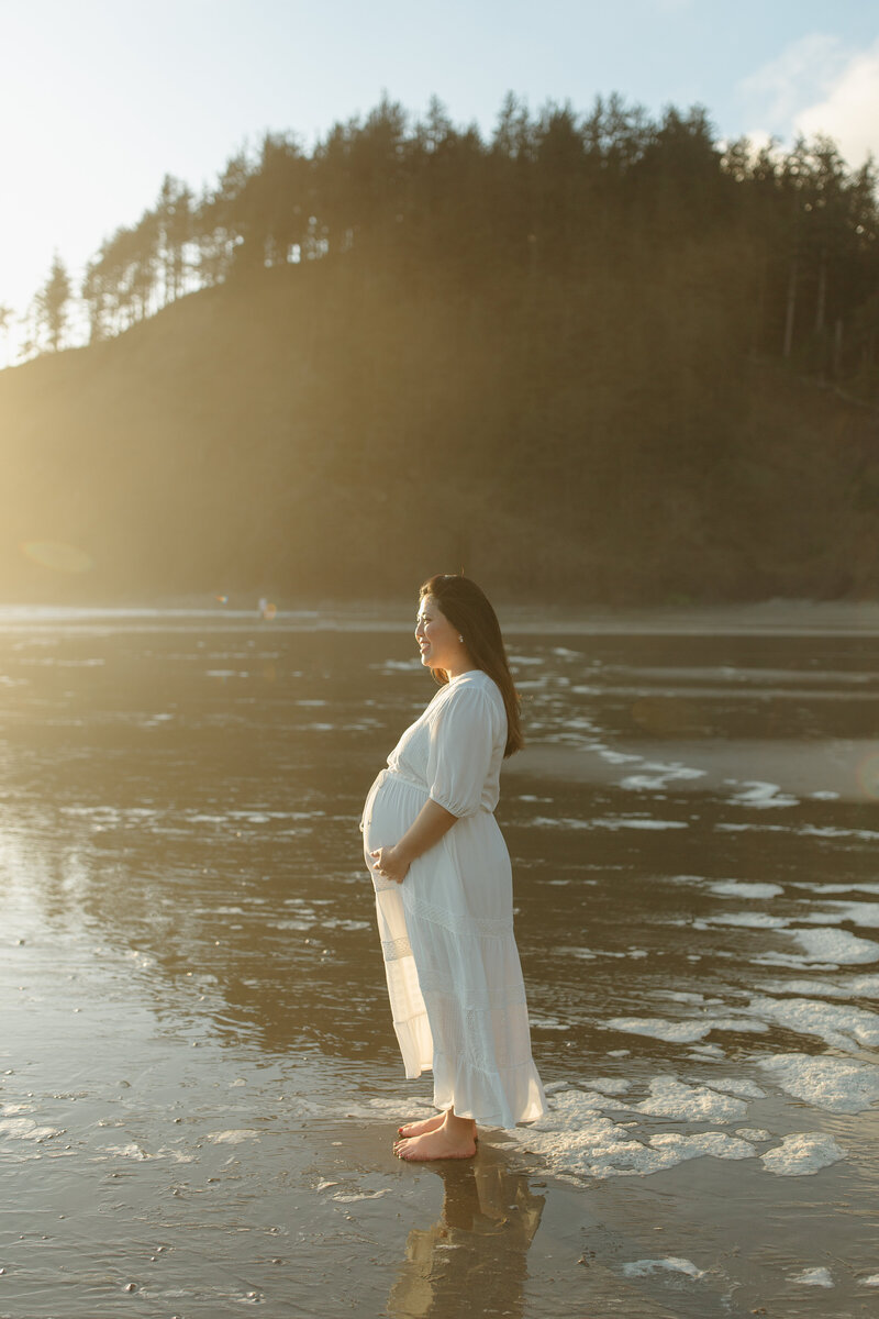 pregnant mother holding belly at sunset at indian beach
