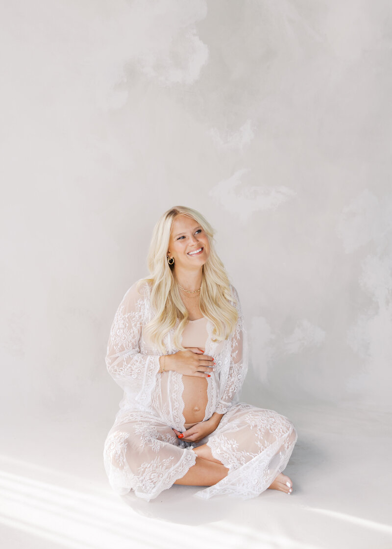 Woman dresssed in white holding her pregnant belly at a minneapolis in studio maternity photo session with angela watts photography