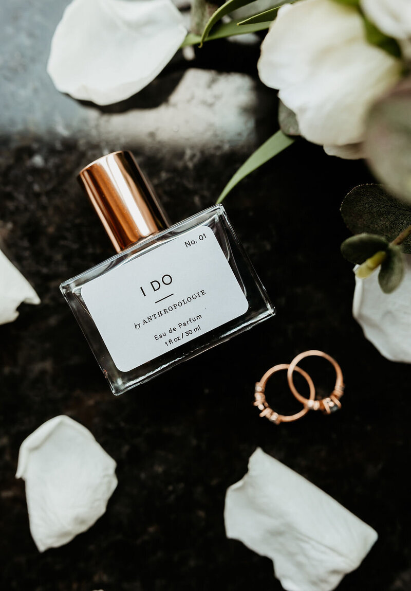 wedding flat lay of perfume with wedding rings and flowers