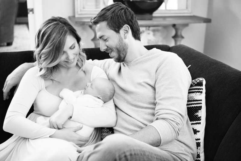 Black and white photo of parents on couch holding baby by Orlando Newborn Photographer