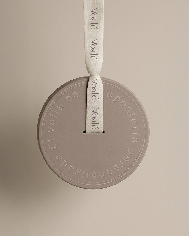 Round, soft-mauve box from Voalé. A cream ribbon, delicately printed with the brand’s name in lavender, threads through the center—capturing Voalé’s refined and artisanal identity.