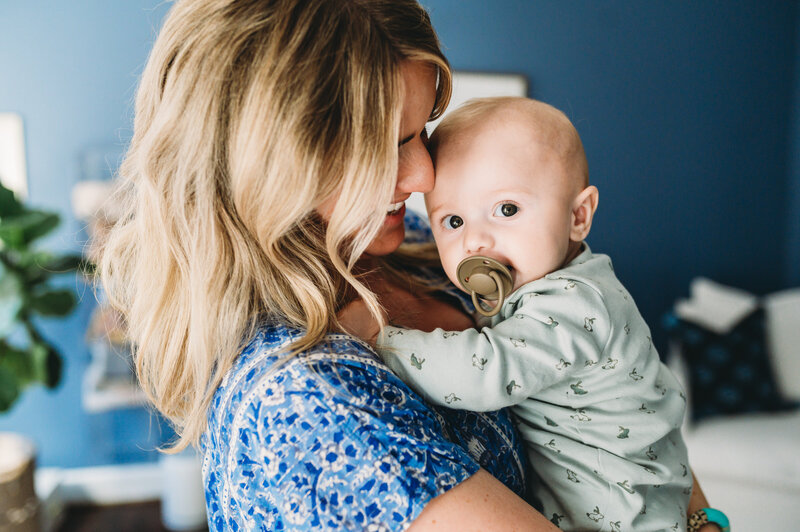 mother wearing blue holding her baby boy with paci in nursery at home