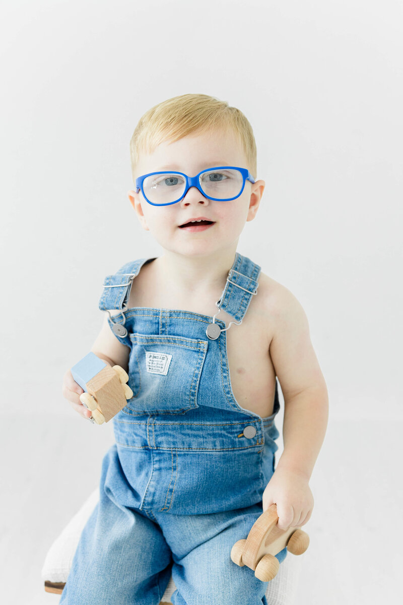 Boy sitting in overalls smiling at camera for milestone photography in mini model rep program