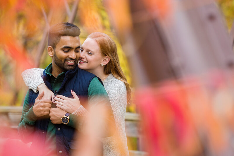 Mixed-race engaged couple standing on an iron bridge in Phoenixville during their engagement session, sharing a romantic moment and highlighting the historic charm of the location.