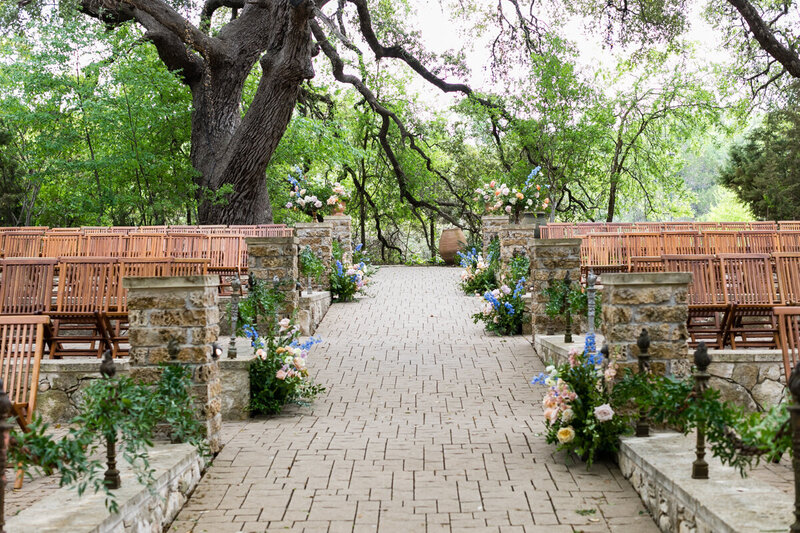 Dreamy outdoor ceremony with lush florals, natural stonework, and oak trees—whimsical setting for nature-loving couples.
