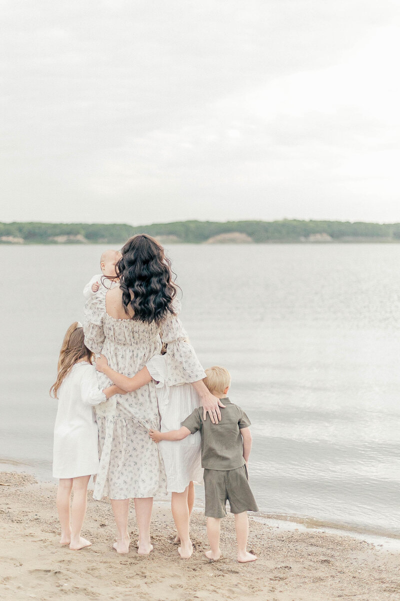 Kansas City mom stands barefoot at the water’s edge, arms wrapped around her four young children.