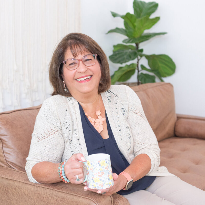 A woman sitting on a couch smiling and holding a mug.