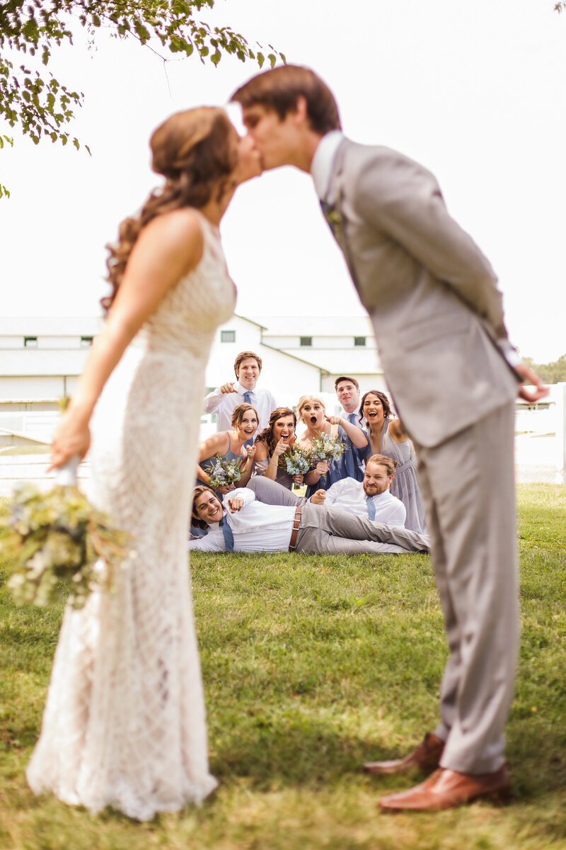 bride and groom kissing while bridal party cheers them on