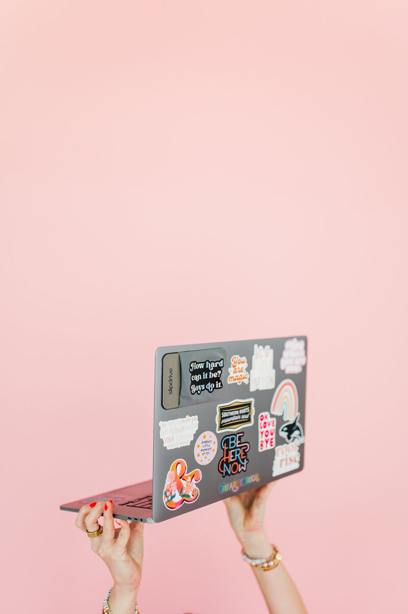 woman holding a laptop covered in stickers promoting strong women, love and empowerment