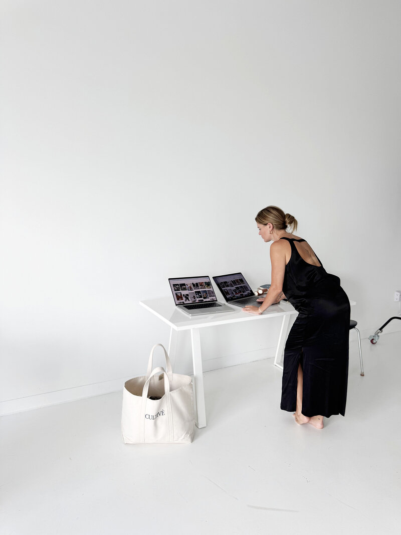 Black and white photo of a young woman wearing protective laser glasses, filming or photographing content as a laser hair removal treatment is performed on a med spa client, capturing a behind-the-scenes moment in a clinical setting.