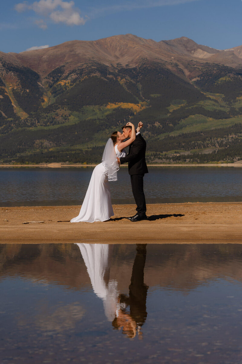 Couple kissing along the banks of an alpine lake in Colorado as their reflection shines
