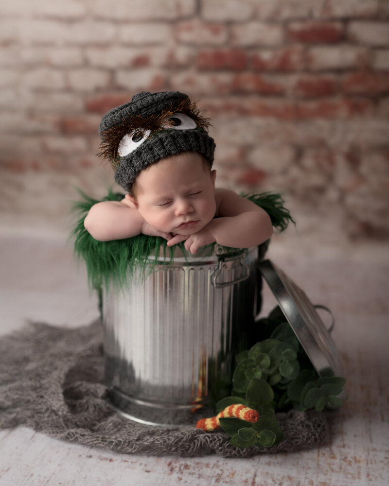 Whimsical Oscar the Grouch newborn session with a metal trash can prop and themed hand-knit hat.