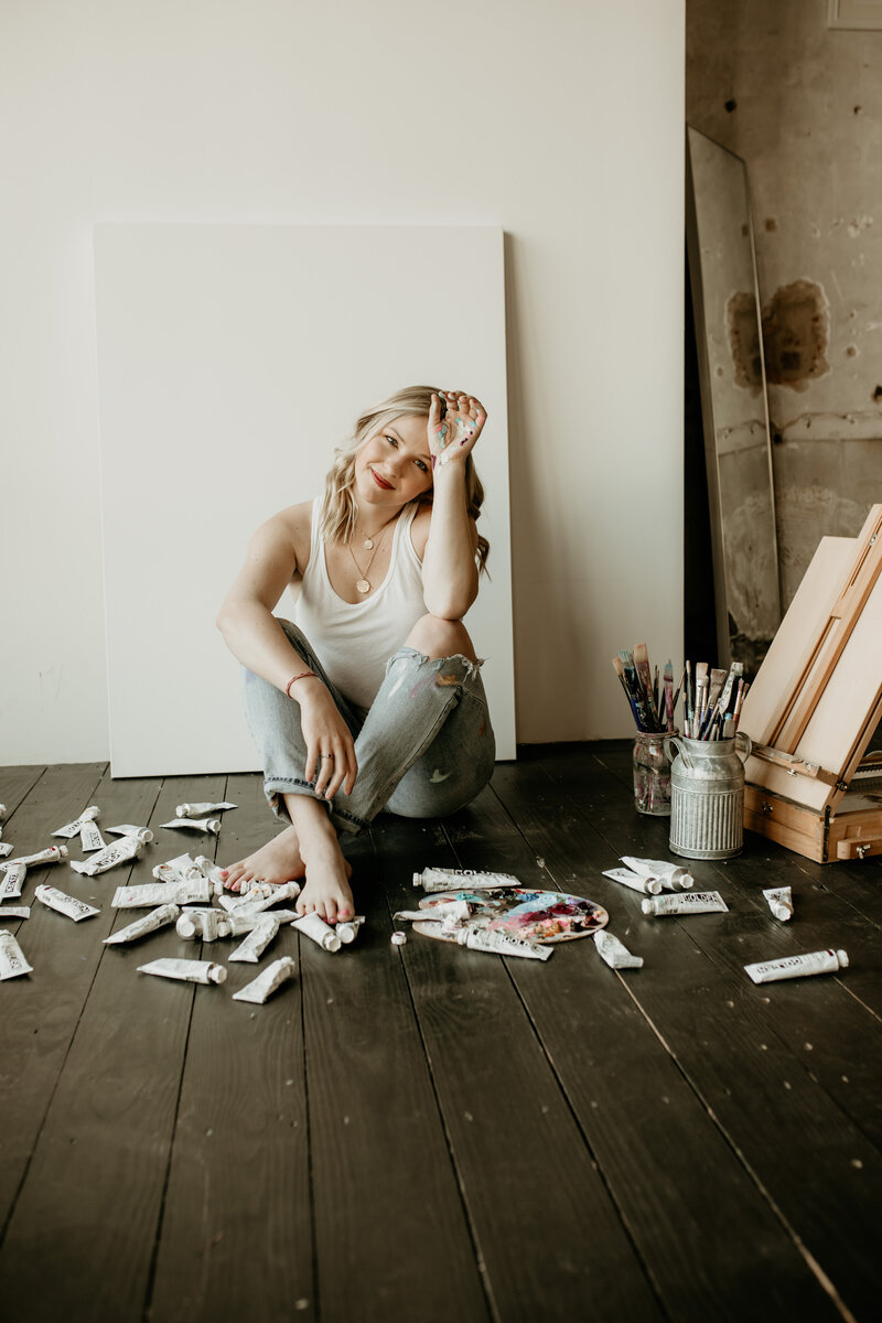 woman sitting on the ground with paintings behind