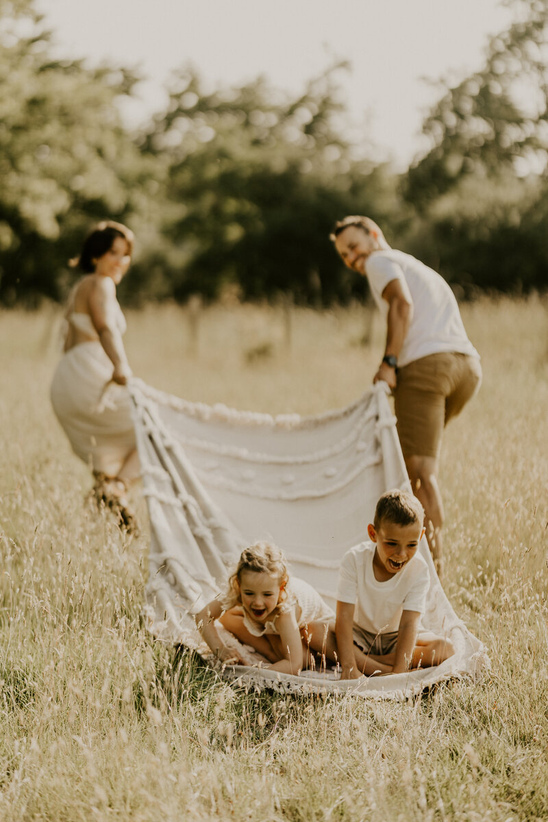 Trois garçons d'âges différents  jouant sous un parasol blanc sur la plage, capturés par Laura, photographe en Vendée.