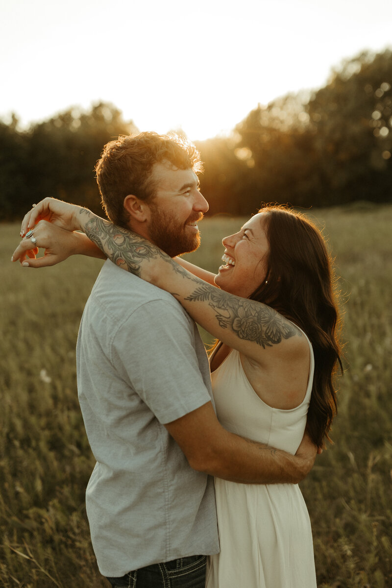 Man embracing his fiancée from behind in a wildflower field at sunset.