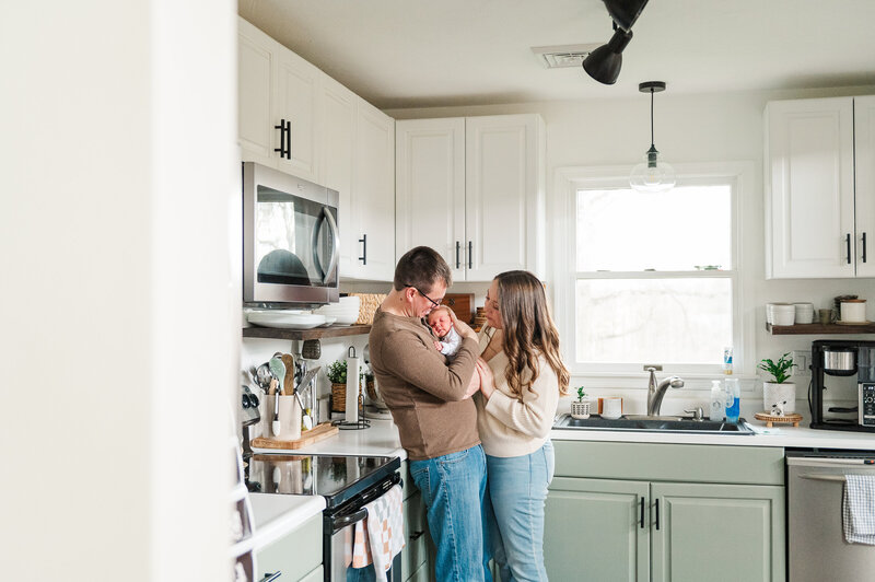 Mom and dad snuggling their newborn in a bright York, PA kitchen during a Day in the Life photography session.