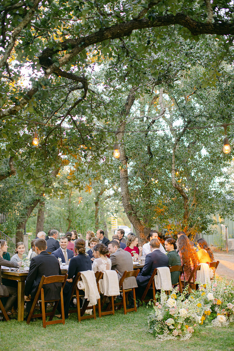 Guests sit outside at a wooden table during a wedding reception at the wayback