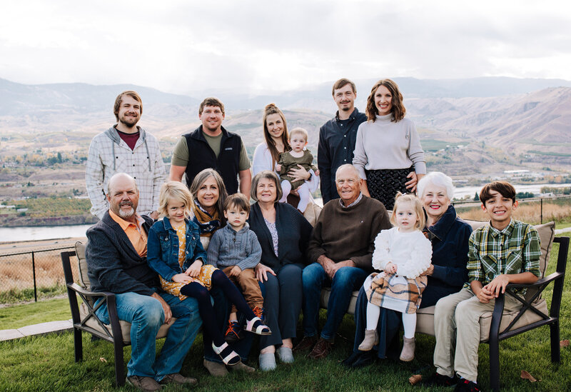 A family with four generations sitting together. In the background, there are tall mountains, trees, and the Columbia River.