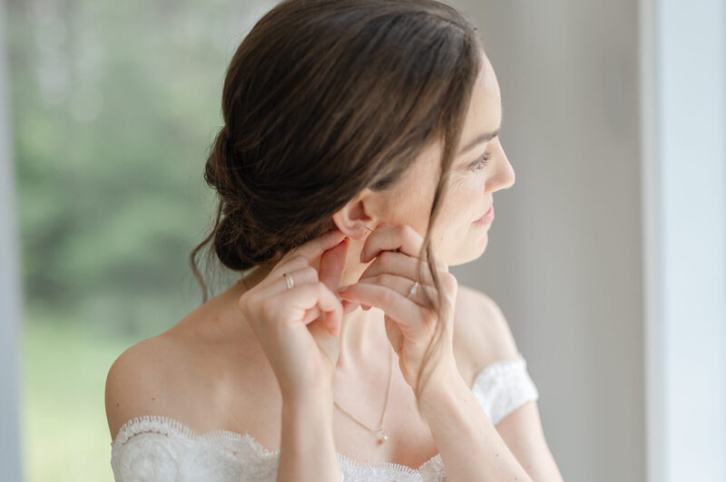 La mariée enfile sa boucle d’oreille avec délicatesse pendant ses préparatifs à Laval, moment élégant et lumineux capturé dans l’intimité d’un mariage raffiné