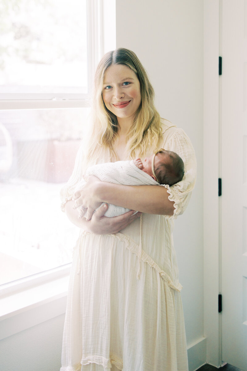 Austin mom whiles holding her newborn baby.