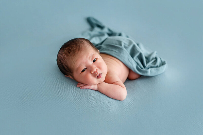 Chinese newborn baby boy on a blue backdrop with a blue wrap on for his newborn photography session in Burlington