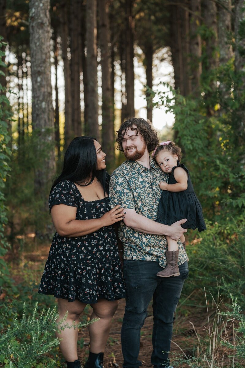 Mother, Husband, and Young Daughter posing for a family photo in the woods