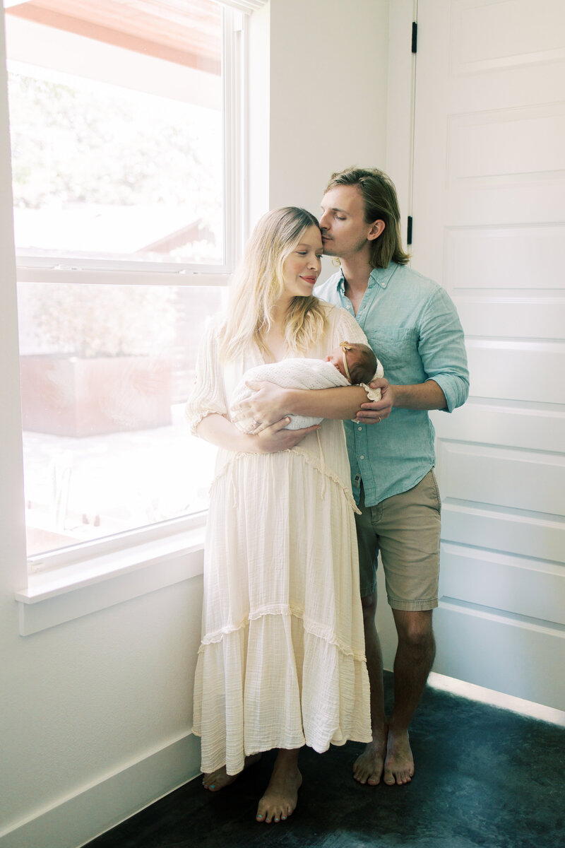 Austin dad kisses wife on the head while she holds their newborn baby.